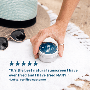 hand picking up tin of sunscreen off a white blanket with customer review from a verified customer