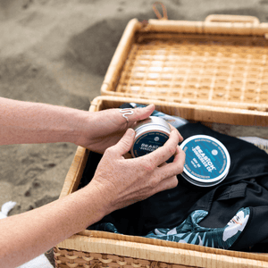 hands holding a tin of sunscreen over a basket holding beach gear