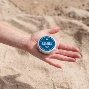 small metal tin with blue label sitting in the palm of a hand with sandy background
